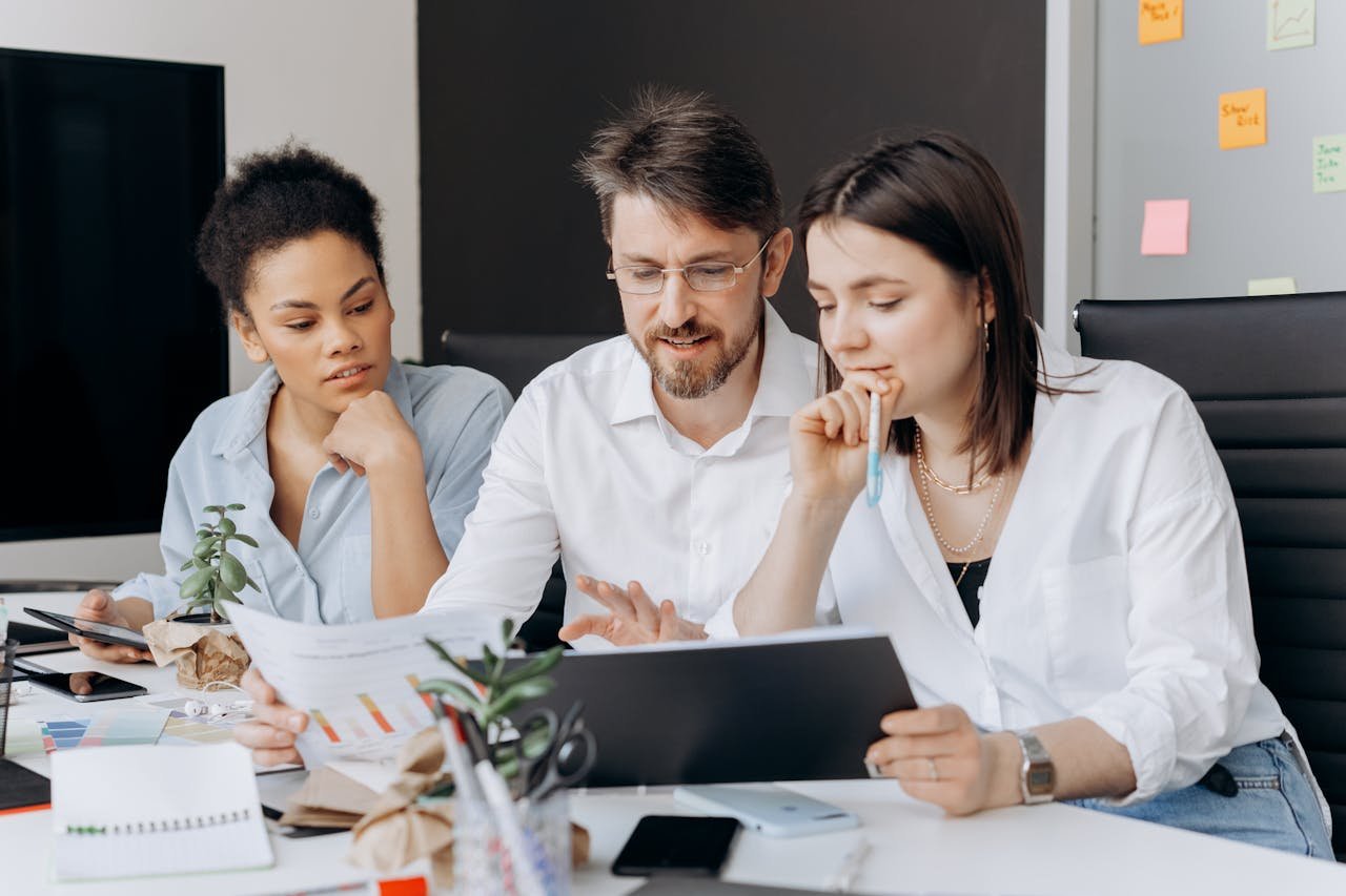 A diverse group of colleagues brainstorm around a laptop and documents in a modern workspace.